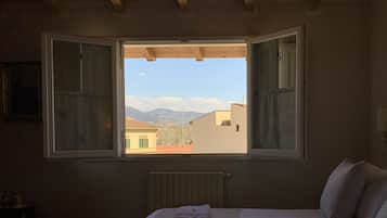 A bedroom with a large window, a bed with a white duvet, and a radiator.