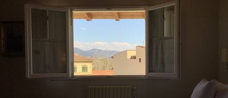 Une chambre avec une grande fenêtre, un lit recouvert d’une couette blanche et un radiateur.