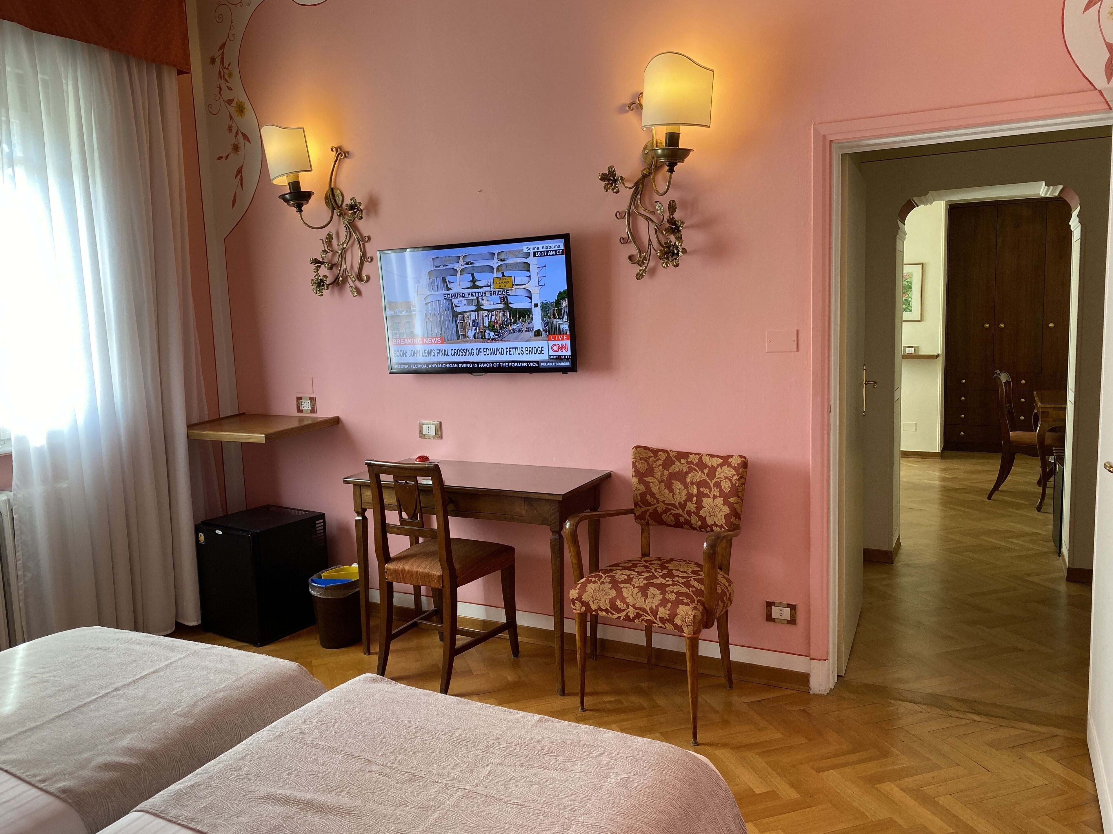 Une chambre d’hôtel avec un téléviseur fixé au mur, un bureau, deux chaises, un lit et un plancher en bois.