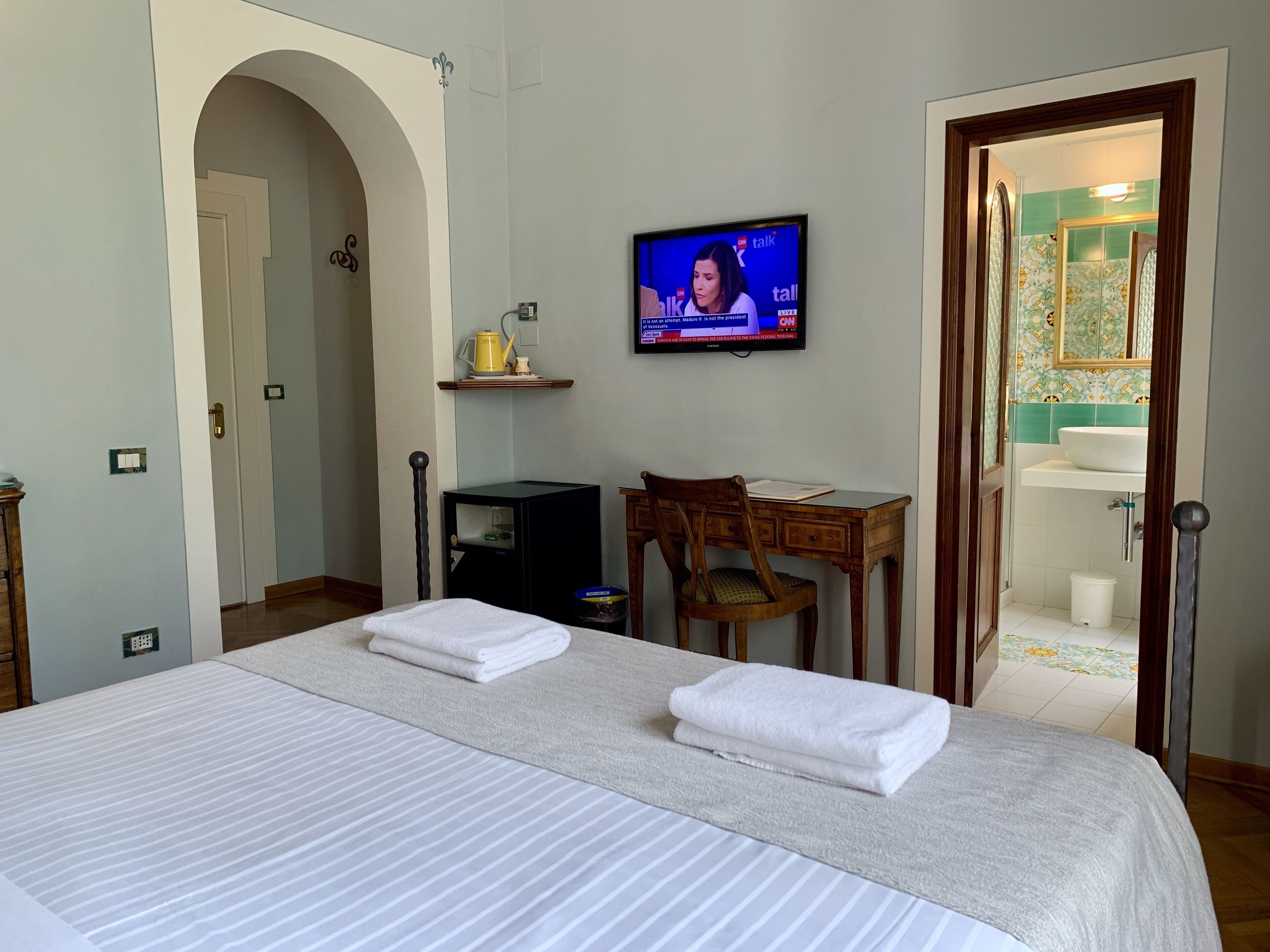 Een hotelkamer met een bed, een bureau, een stoel, een televisie en een badkamer die door een geopende deur zichtbaar is.