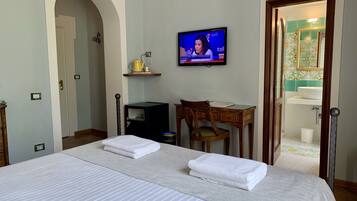 Een hotelkamer met een bed, een bureau, een stoel, een televisie en een badkamer die door een geopende deur zichtbaar is.