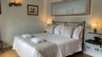 A neatly made bed with white linens and a beige throw blanket, two wall-mounted lamps, a framed painting, and a large landscape painting above the bed.