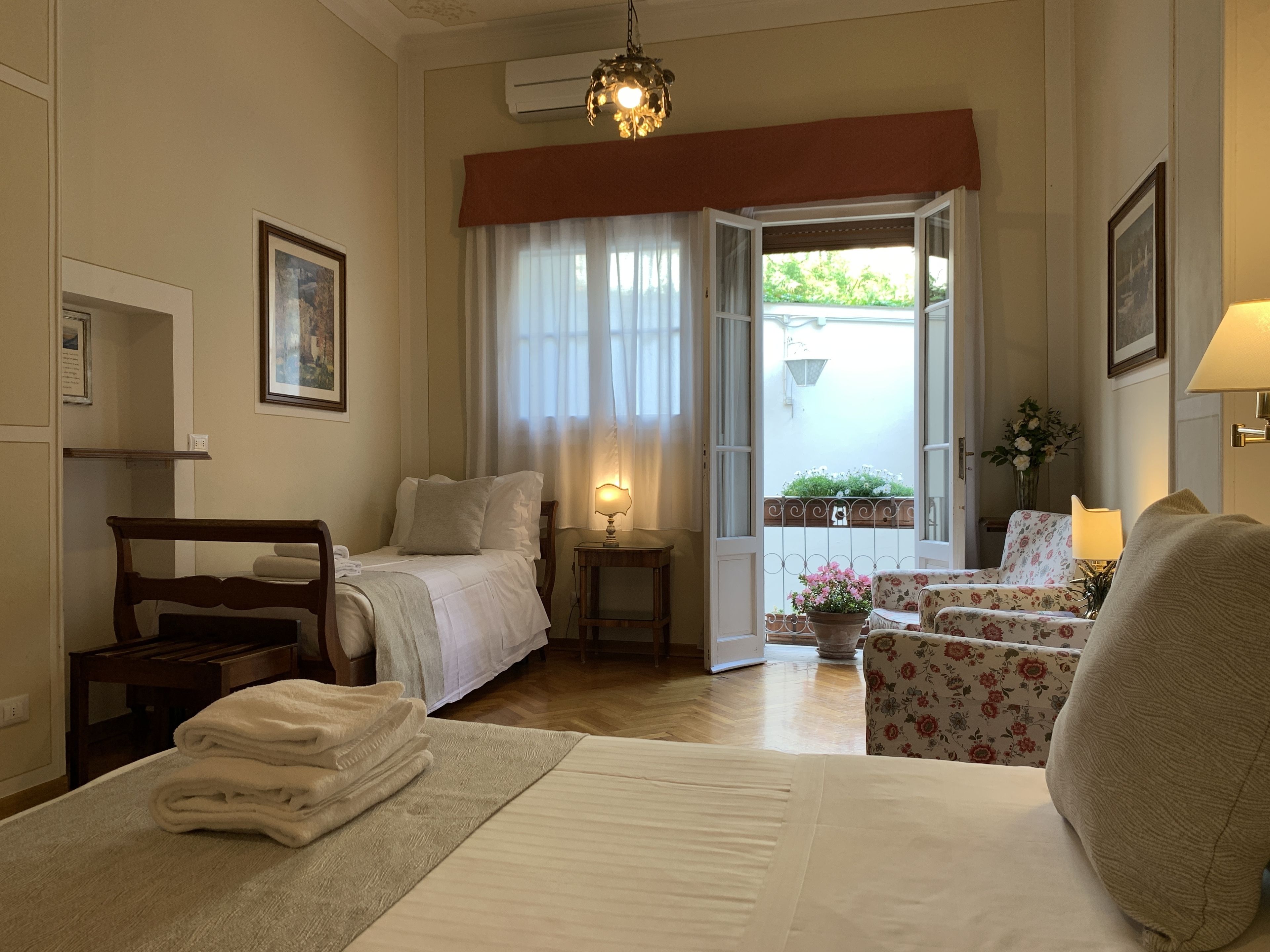 A hotel room with a bed, a chair, a table, a lamp, and a view of the outside.