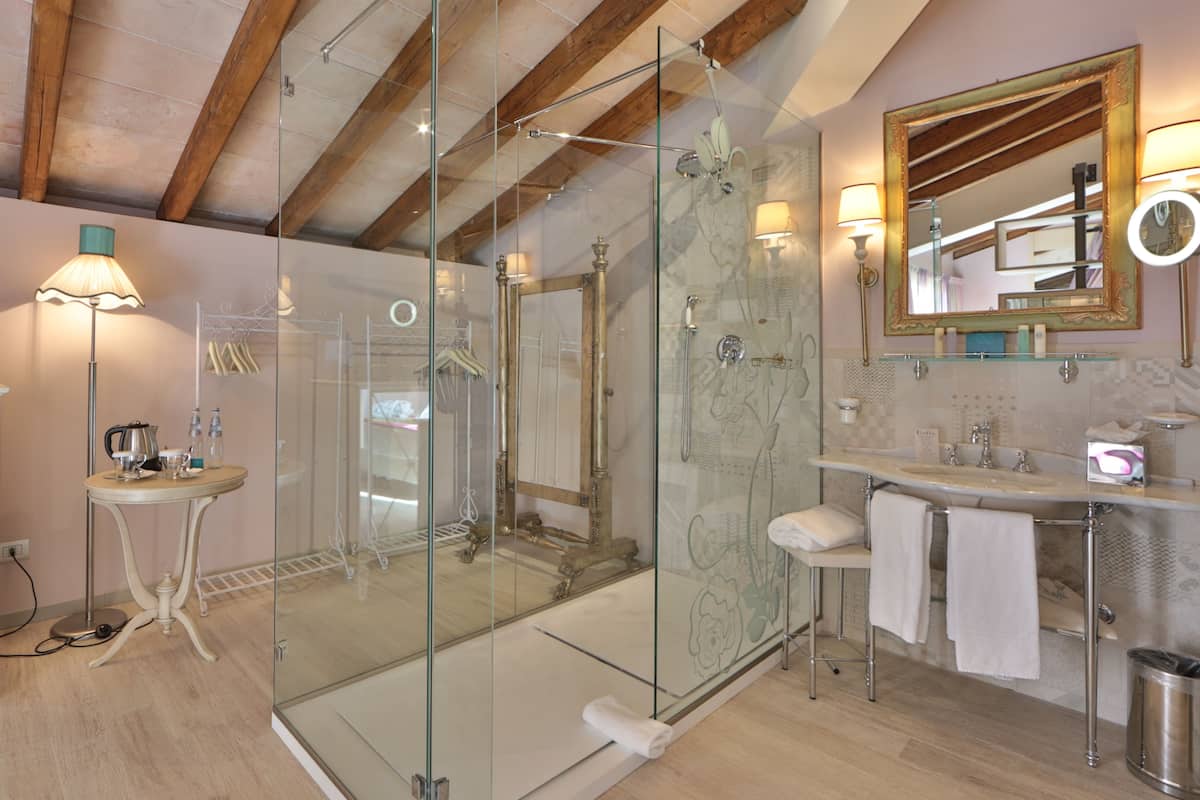 A modern bathroom with a glass shower enclosure, a vanity with a mirror, and a small table with a lamp.