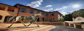 Un cortile con una statua equestre, un edificio con finestre ad arco e una panchina in pietra.