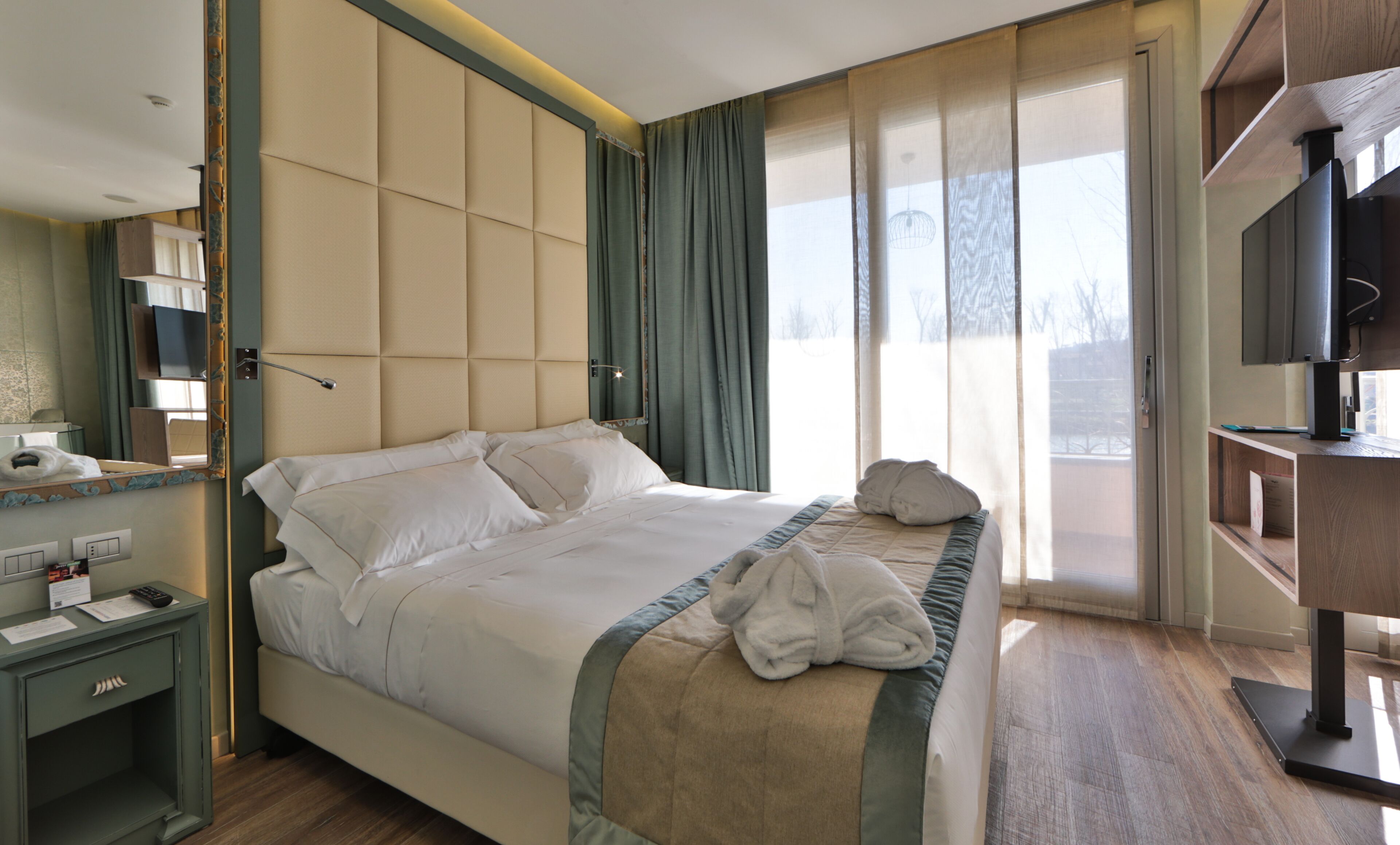 Une chambre d’hôtel avec un grand lit, une table de chevet, un miroir, une télévision et une vue sur l’extérieur.