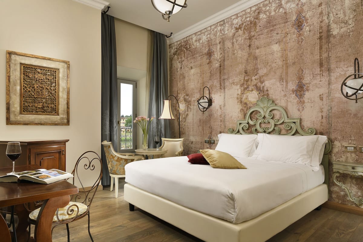 A bedroom with a large bed, a desk with a chair, a window with a view, and a decorative wall.