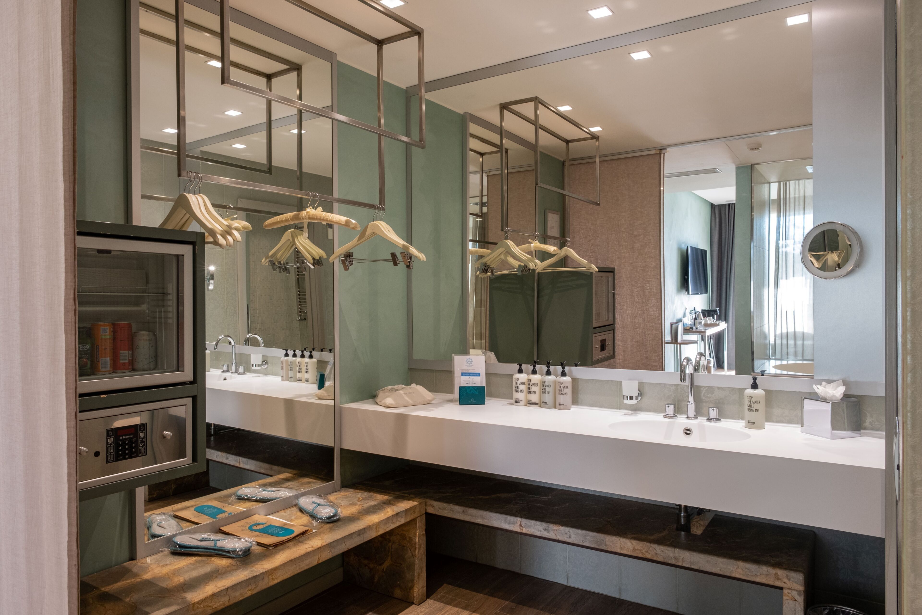Een moderne badkamer met een grote spiegel, een wastafelmeubel en een bankje met toiletartikelen.
