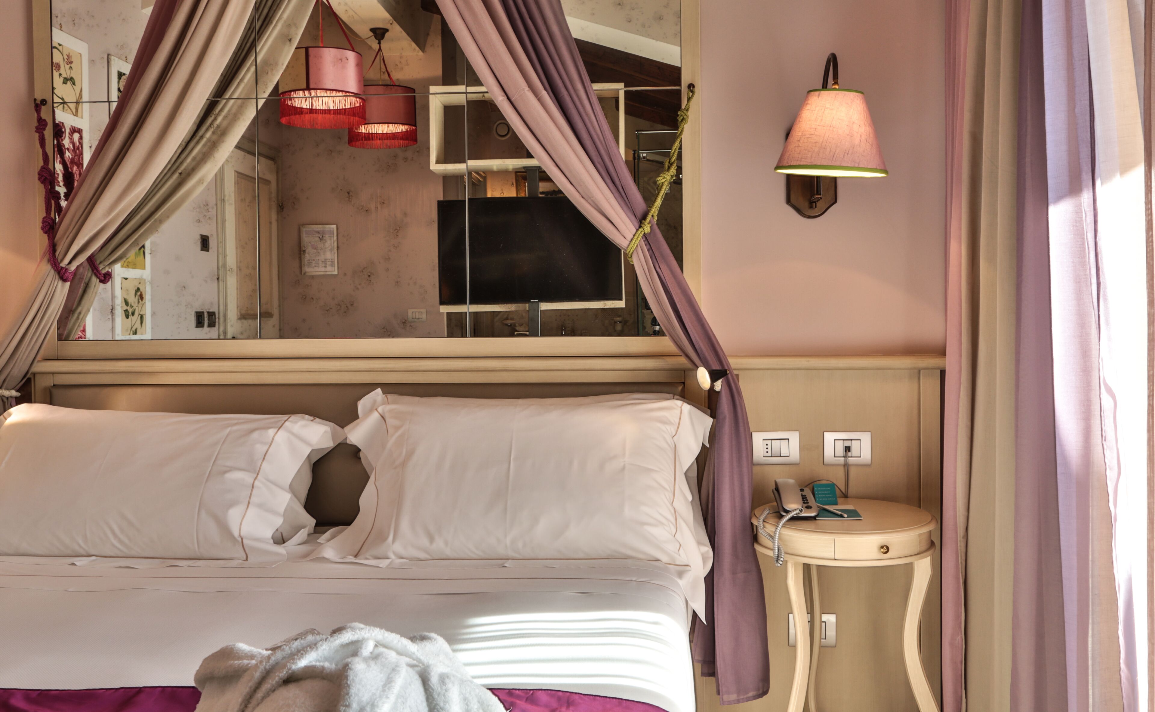A bed with a canopy, a bedside table with a phone, and a wall-mounted light fixture.