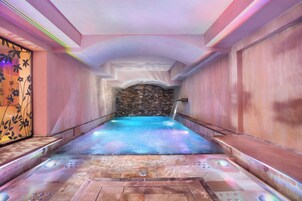 Una spa con una parete in pietra, una piscina illuminata di blu e una panca in legno.