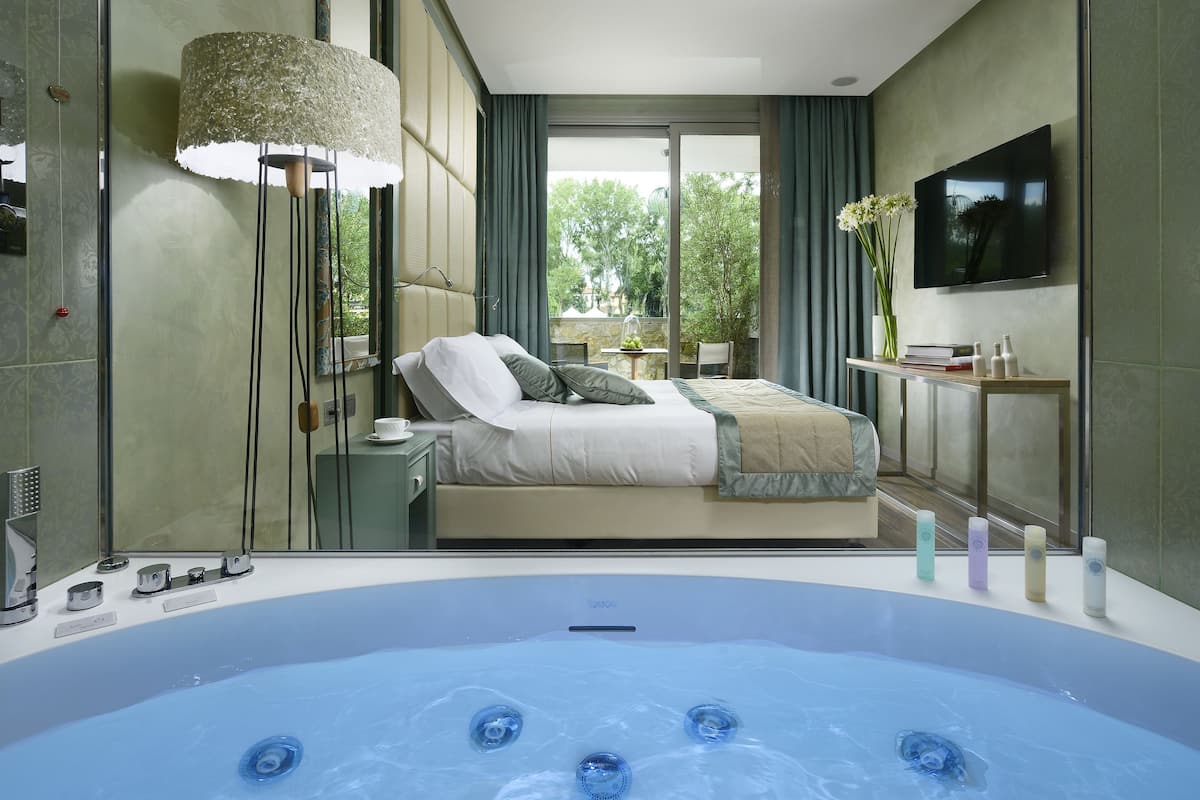 A modern bedroom with a large bed, a glass-enclosed balcony, a TV, and a hot tub.