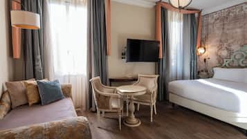 A hotel room with a bed, a sofa, a dining table with chairs, a TV, and a lamp.