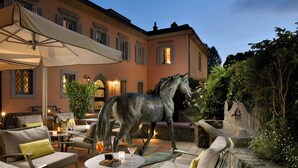 A patio area with outdoor seating, a horse statue, and a building with warm lighting. - Hotel Ville sull'Arno - Preferred Hotels & Resorts (Florence)