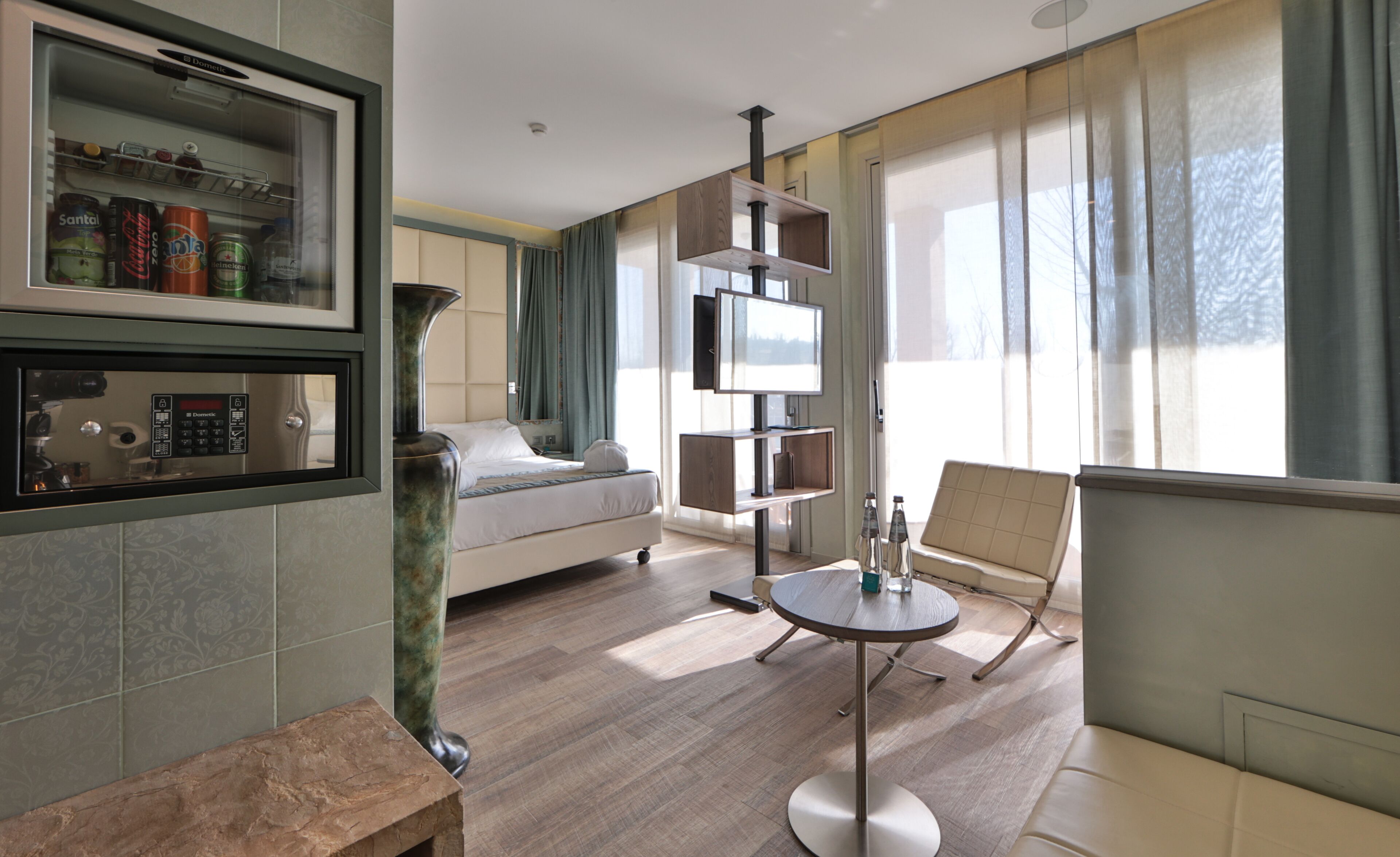 Una habitación de hotel moderna con una cama, una mesita redonda pequeña, un sofá, un televisor integrado y un minibar.