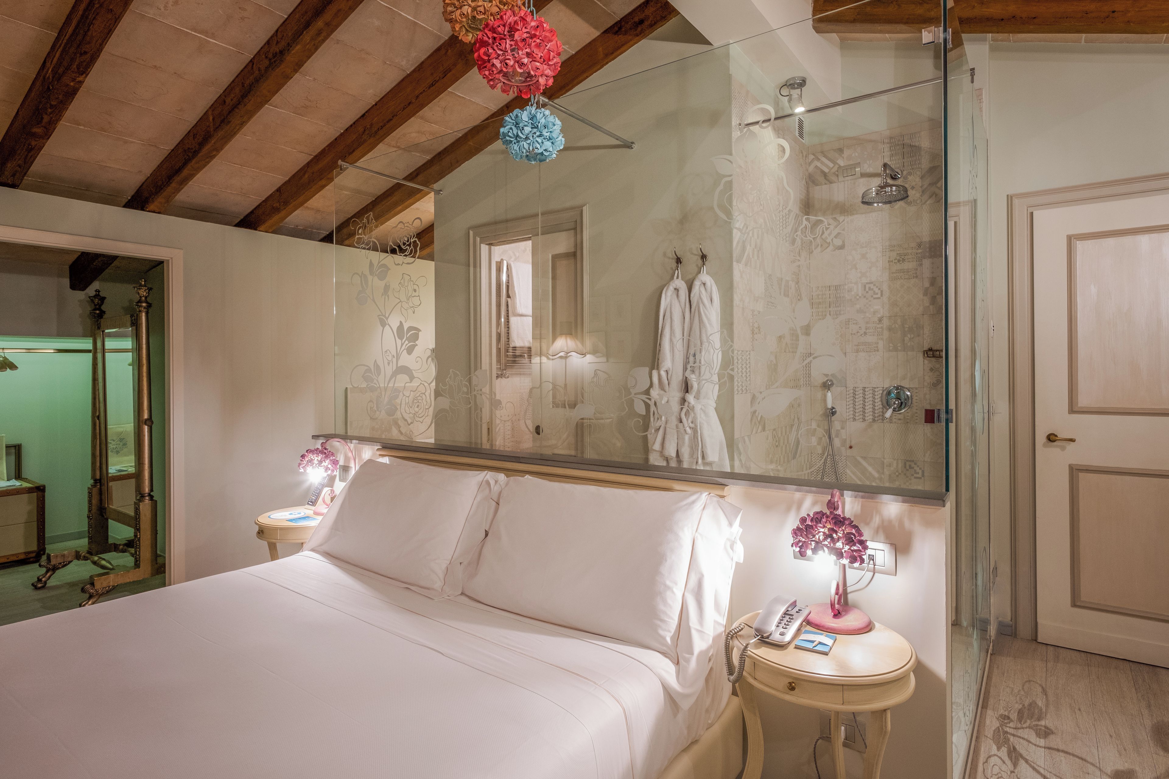 Ein Hotelzimmer mit einem großen Bett, einem Nachttisch mit Lampe, einem Spiegel und einer Duschkabine.
