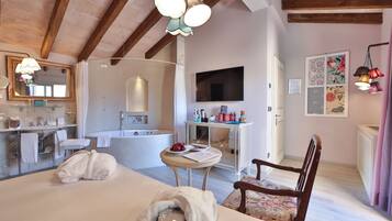 Hotelkamer met een groot bed, een zithoek met een fauteuil, een kleine tafel, een badkuip, een wastafel met spiegel, en een flatscreen televisie aan de muur.