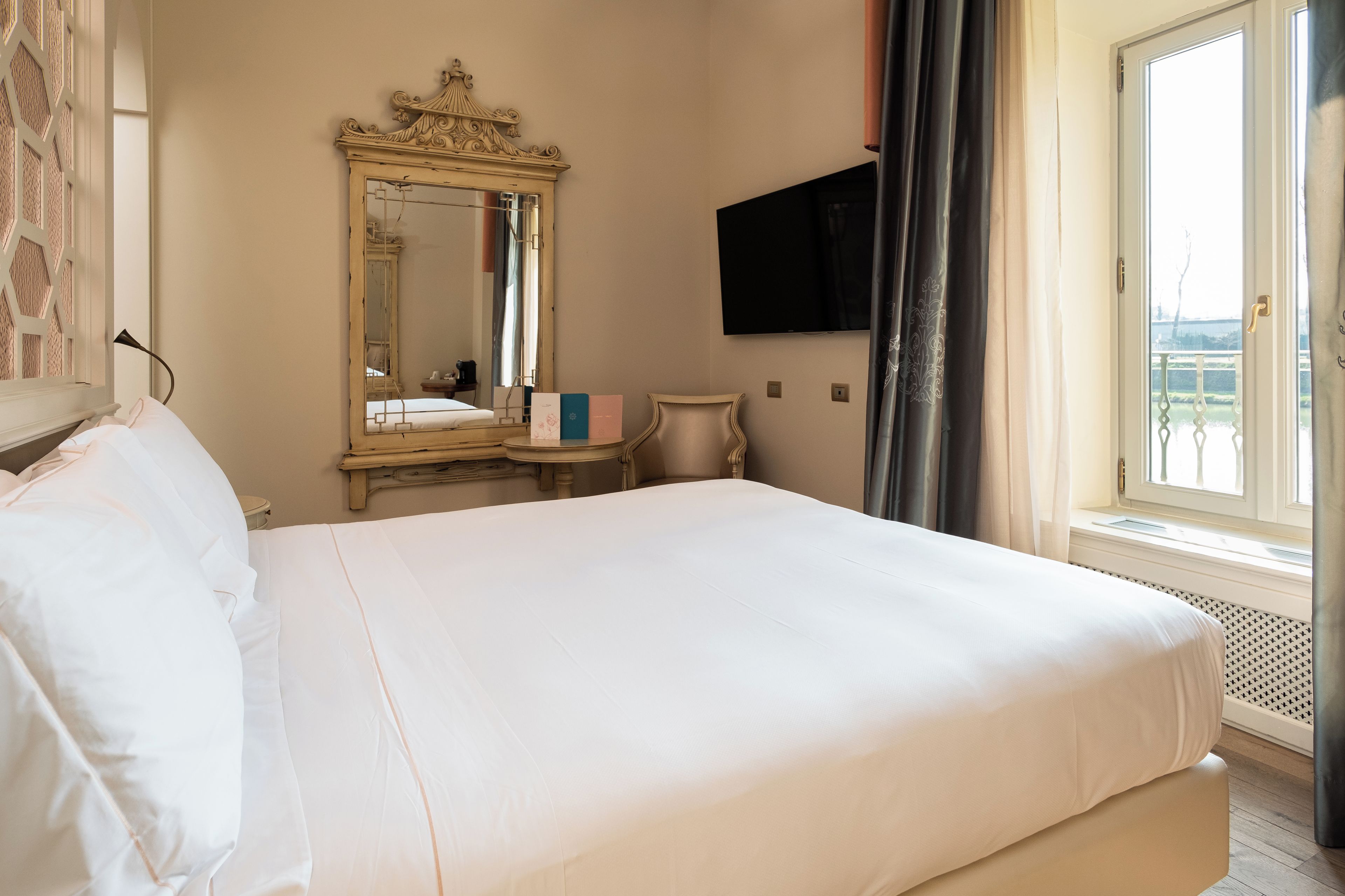 Ein Hotelzimmer mit einem großen Bett, einem Spiegel, einem Flachbildfernseher und Blick ins Freie.