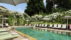 A pool area with lounge chairs and umbrellas, surrounded by lush greenery and white flowers.