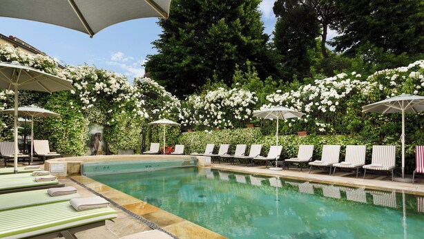 A pool area with lounge chairs and umbrellas, surrounded by lush greenery and white flowers. - Hotel Ville sull'Arno - Preferred Hotels & Resorts (Florence)