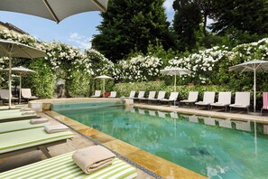 A pool area with lounge chairs and umbrellas, surrounded by lush greenery and white flowers. - Hotel Ville sull'Arno - Preferred Hotels & Resorts (Florence)