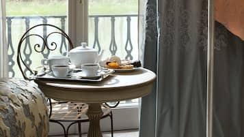 Un comedor con una mesa dispuesta para el té, vista a un parque a través de una ventana y una cortina con estampado floral.