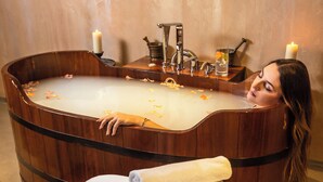 A woman relaxing in a wooden bathtub with candles, surrounded by towels and a tray of flowers. - Hotel Ville sull'Arno - Preferred Hotels & Resorts (Florence)