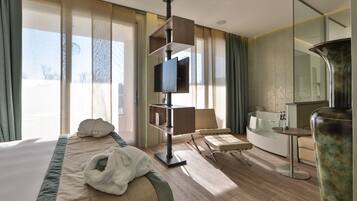 Habitación de hotel con cama, televisión, escritorio, silla, sofá y un ventanal grande.
