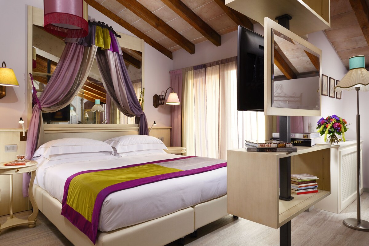 Una habitación de hotel con una cama grande, un escritorio con libros, un televisor y un espejo.