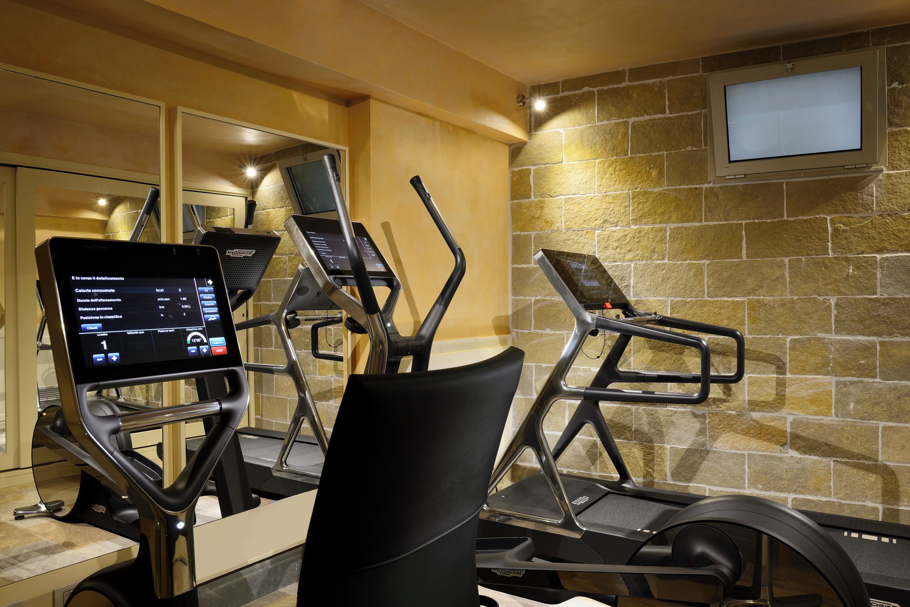 Un gimnasio con equipo de ejercicio, incluyendo cintas de correr y una máquina elíptica, con pantalla digital para registrar entrenamientos.