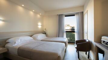 Quarto de hotel com duas camas, uma escrivaninha e uma cadeira. Possui uma varanda com vista para a cidade.