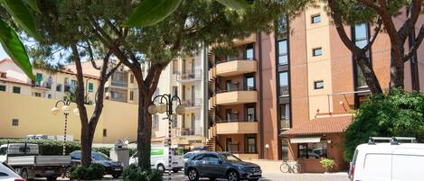 Una àrea de pàrquing amb un cotxe, una furgoneta i un camió. Hi ha arbres i un edifici amb balcons al fons.