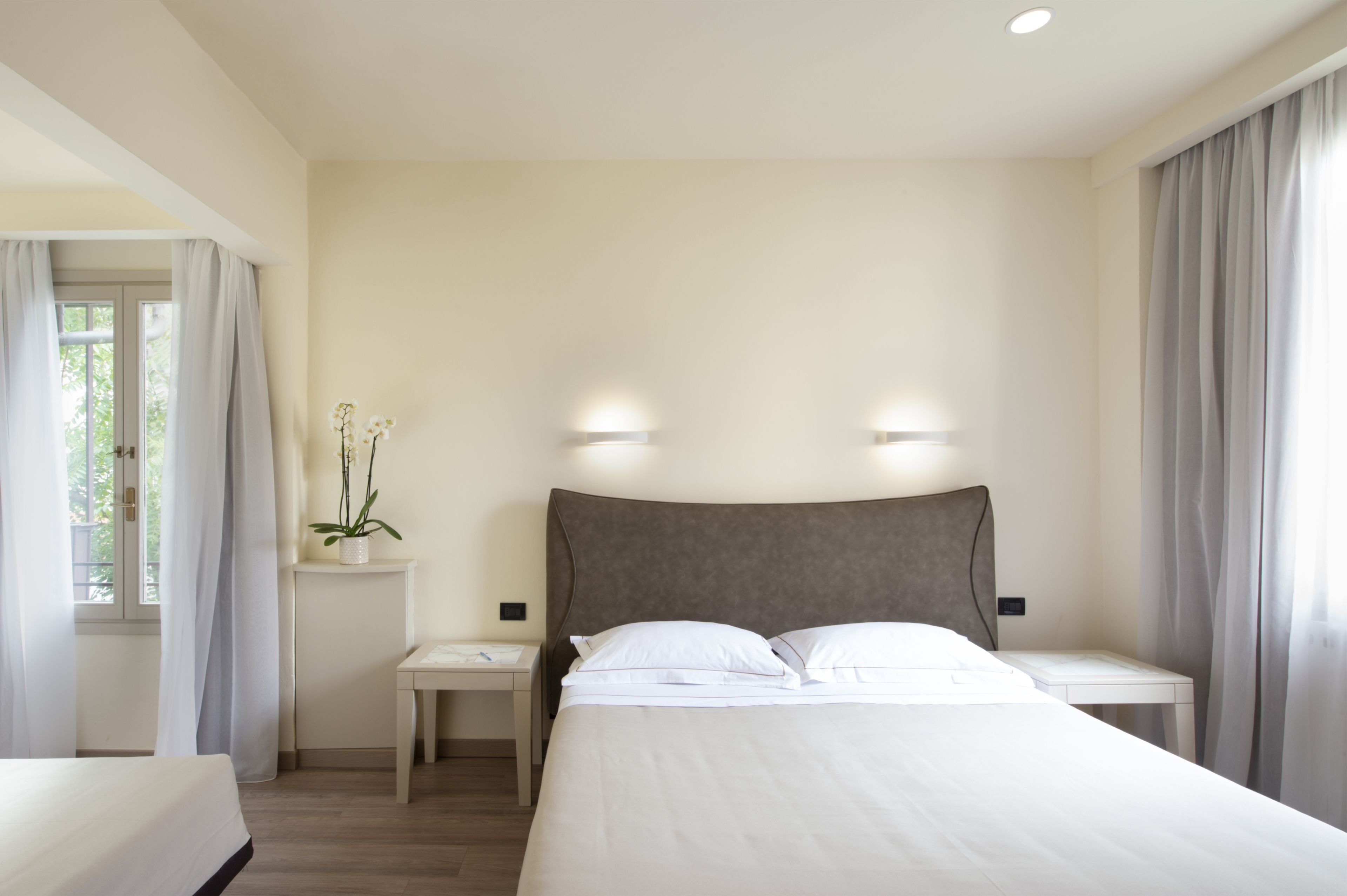 A hotel room with a large bed, bedside tables, a small desk, and a potted plant.