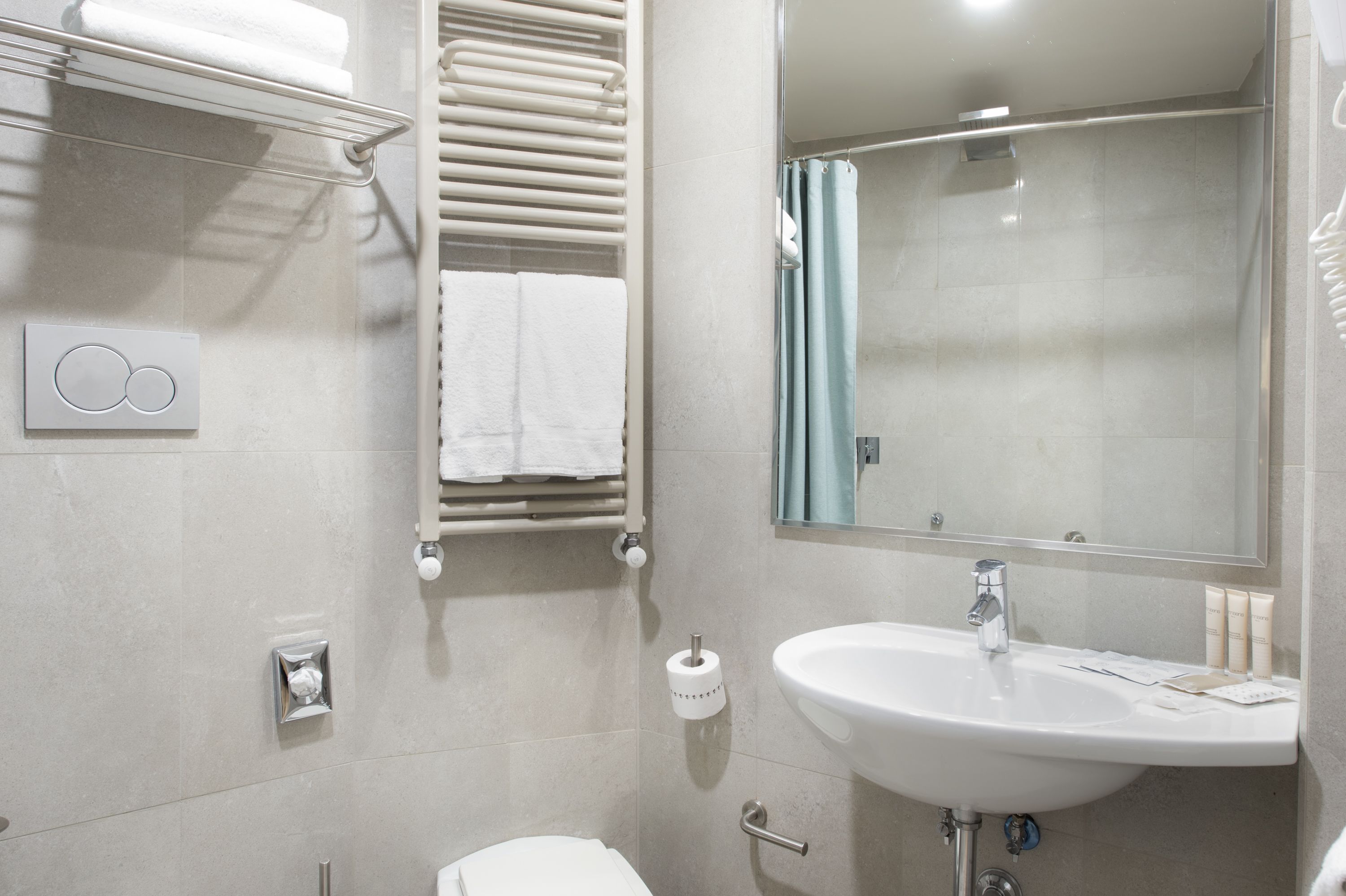 A modern bathroom with a white sink, a mirror, a towel rack, and a shower curtain.