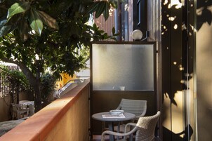 Un balcone con tavolo e sedie, un pannello in vetro satinato e vista su un edificio.