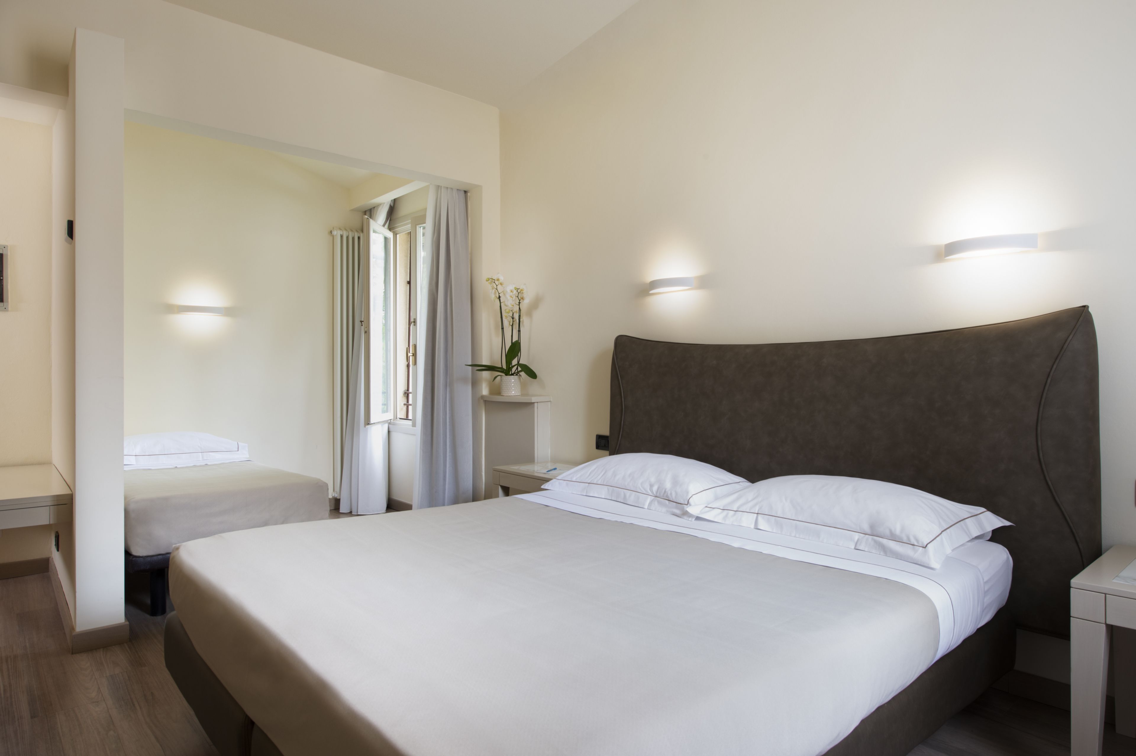 Quarto de hotel com uma cama grande, duas mesas de cabeceira, um criado-mudo e uma janela com cortinas.