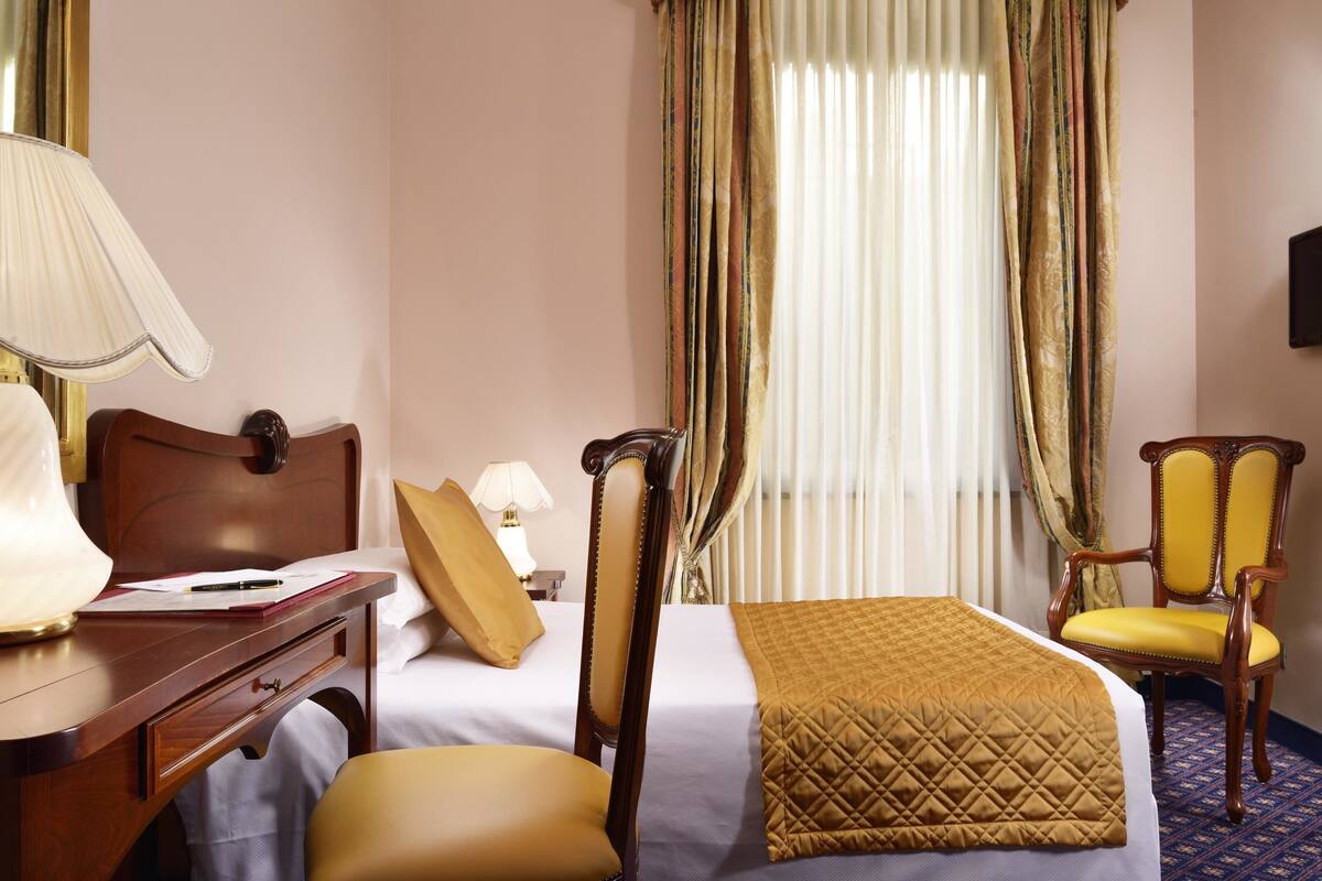 Ein Hotelzimmer mit Bett, Schreibtisch mit Lampe, Stuhl und Fernseher.