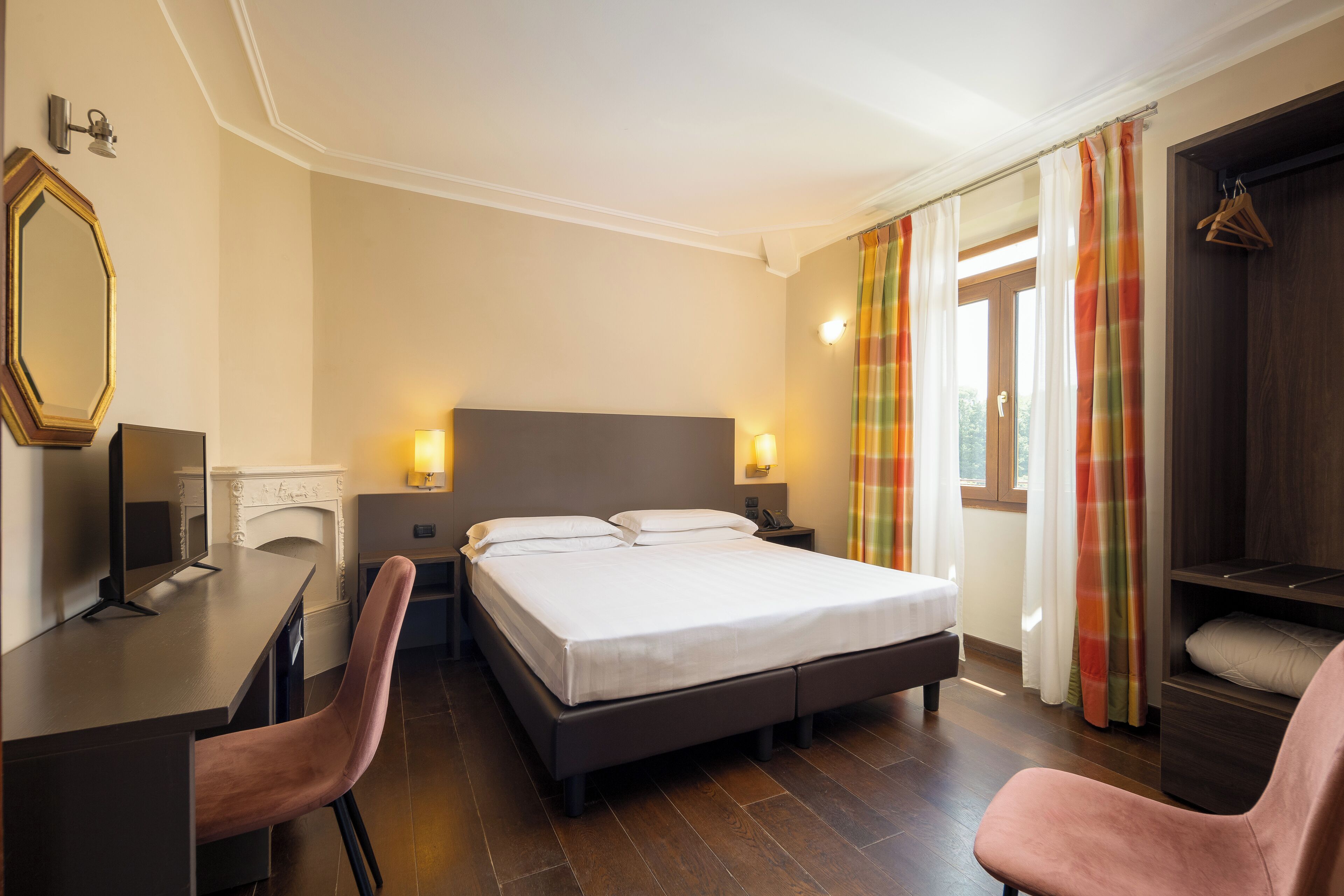 Una habitación de hotel con cama, escritorio, silla, armario y espejo.