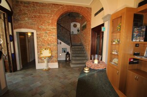 Una hall con parete in mattoni, una scala, una reception e un mobile in legno con oggetti esposti.