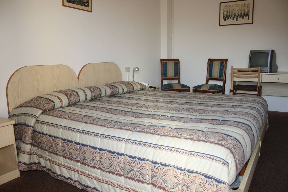 Un dormitorio con una cama grande, dos sillas, un escritorio con una computadora y un televisor.