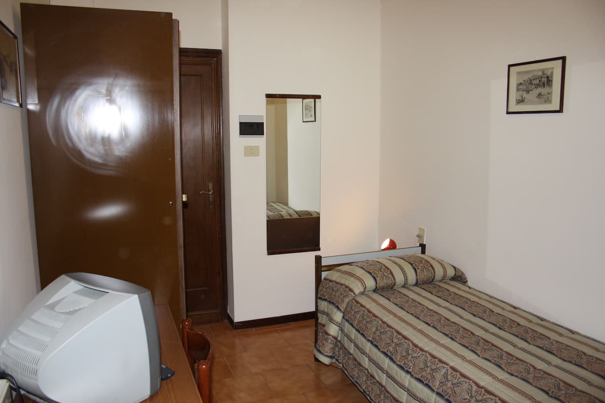 Un dormitorio con una cama, un escritorio con computadora, un espejo y una puerta.