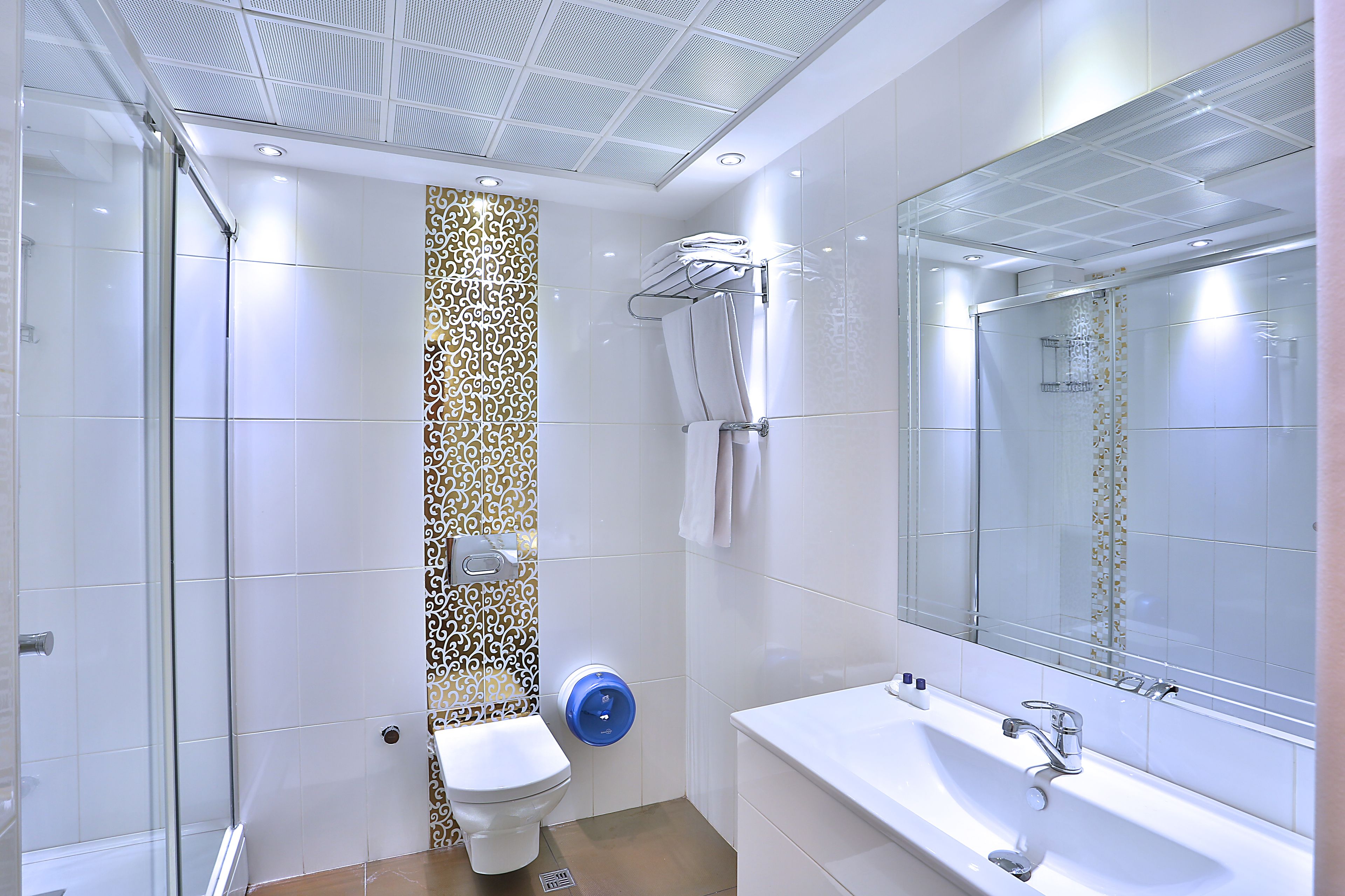Un baño moderno con cabina de ducha de vidrio, inodoro blanco, lavamanos con espejo y azulejos estampados en la pared.