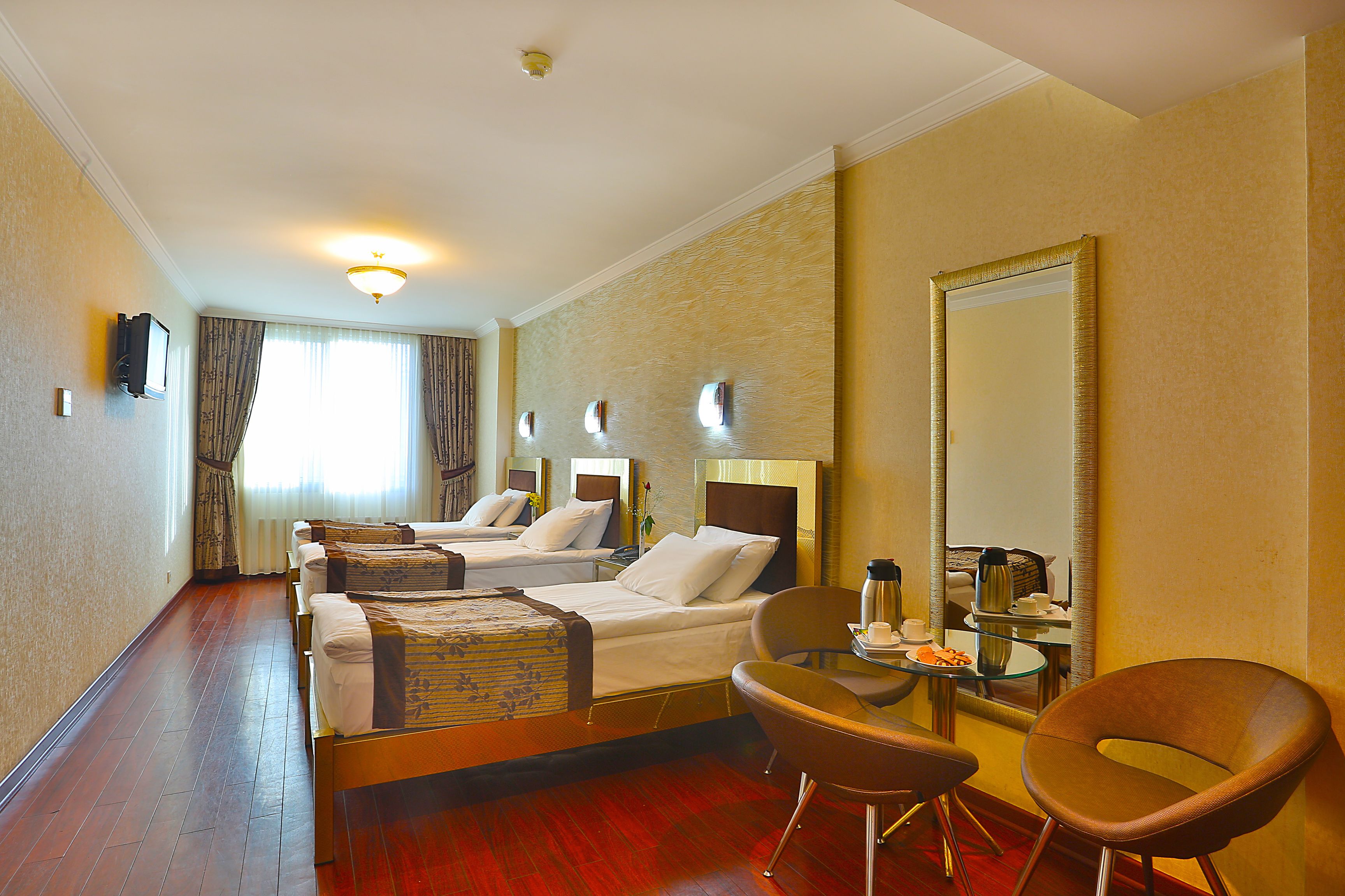A hotel room with two beds, a sitting area with a chair and a table, and a large mirror on one wall.