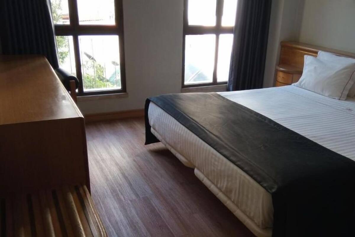 A bedroom with a bed, a wooden nightstand, and a window with curtains.