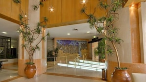 Un hall d’entrée spacieux au design moderne, agrémenté d’un escalier central, de grands pots de plantes et d’une fresque murale décorative.