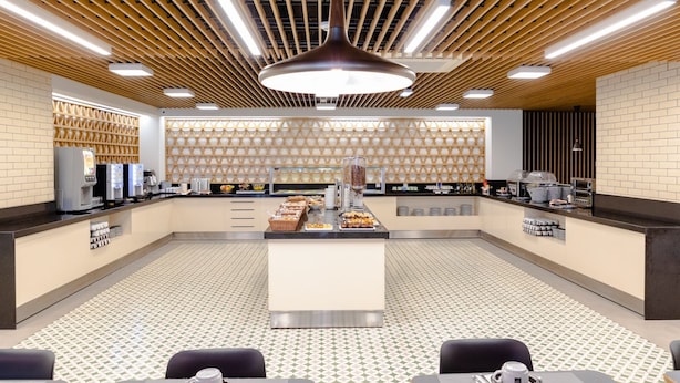 Un espace moderne dédié au petit-déjeuner, avec un comptoir central où les plats sont présentés, des sièges et un sol à motifs.