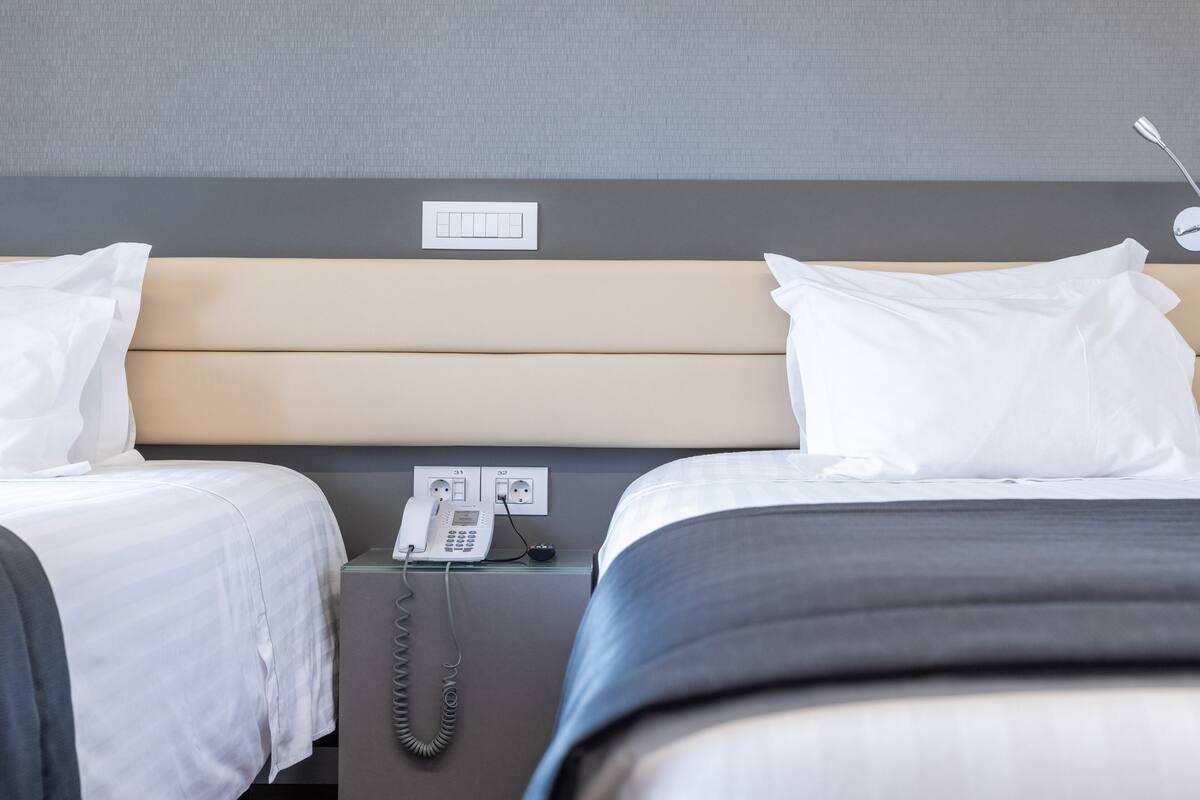 A hotel room with two beds, a bedside phone, and a power outlet on the nightstand.