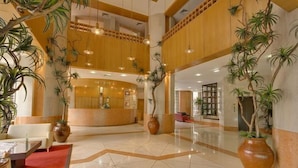 Un hall d’entrée spacieux avec un plafond haut, des éléments décoratifs en bois et de grandes plantes en pot.
