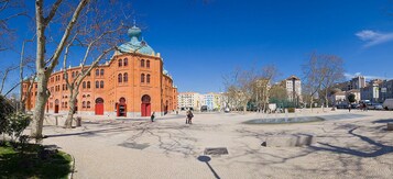 A spacious public square with a prominent red building featuring domes and arched windows.