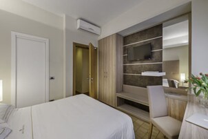 Una camera d'albergo con un letto, una scrivania con una sedia, una TV a muro e un armadio.