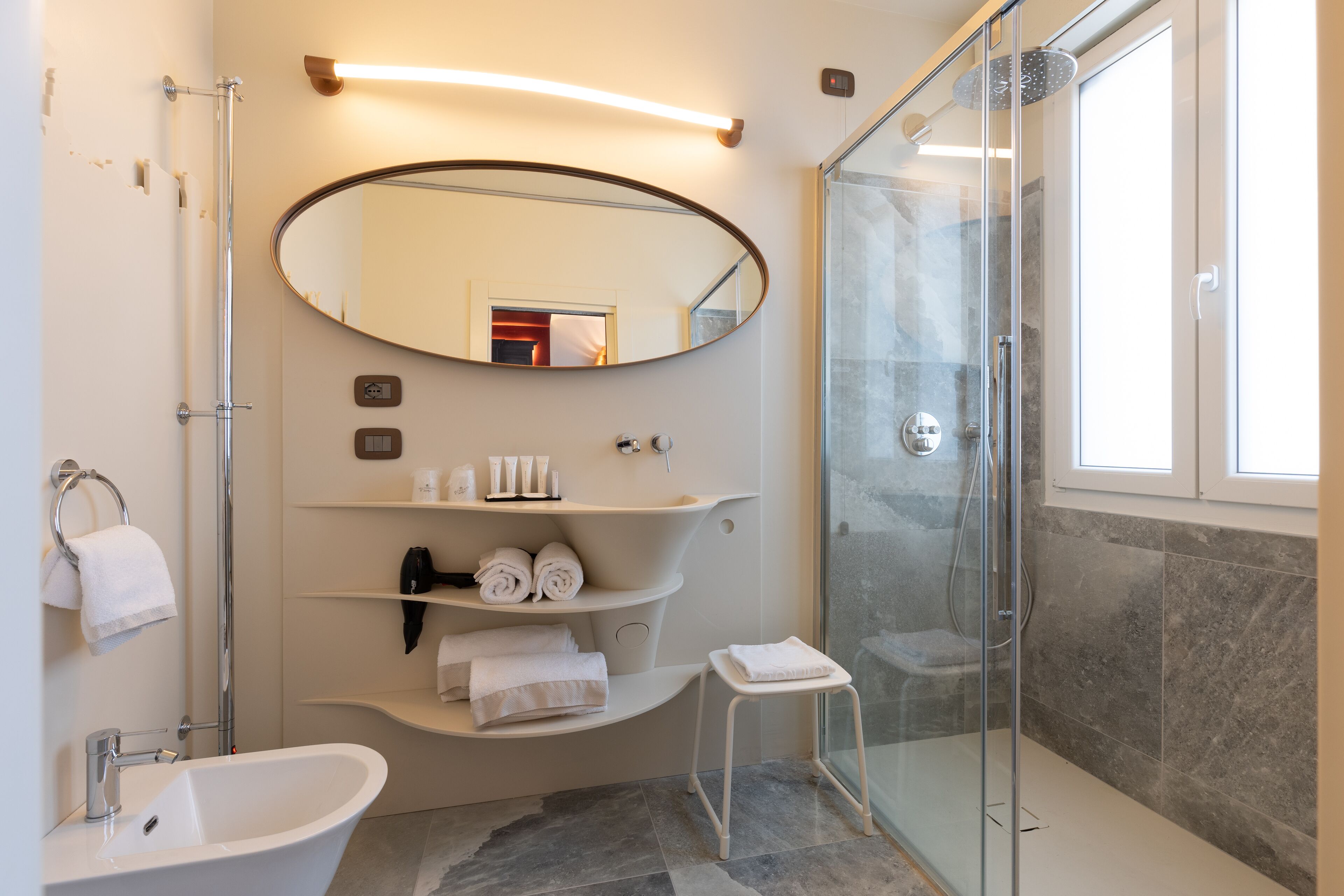 A modern bathroom with a freestanding bathtub, a glass-enclosed shower, a vanity with a mirror, and a small stool.